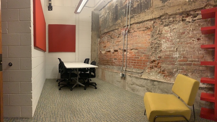 American Underground Office with white cinder block walls and exposed brick wall with conference table, yellow chair, and red bookshelf.